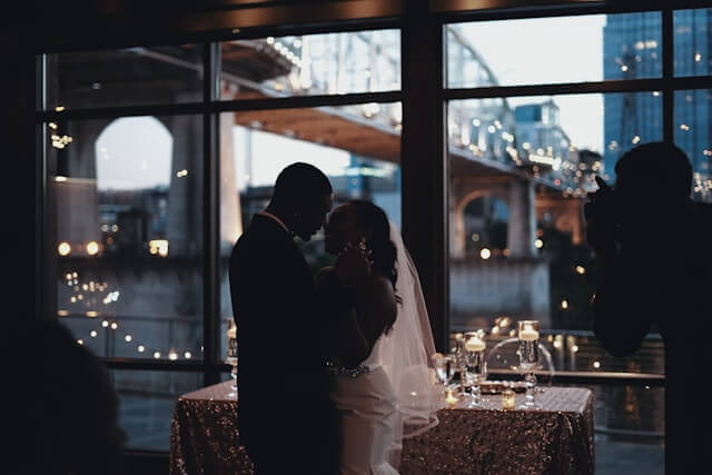 bride and groom kissing in front of a window with lights